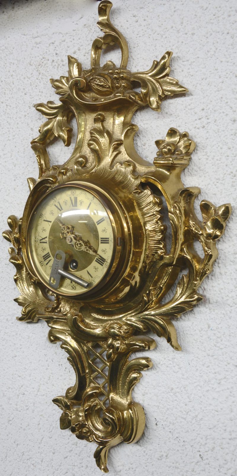 Een wandklok van verguld brons in Lodewijk XV-stijl. Met sleutel.