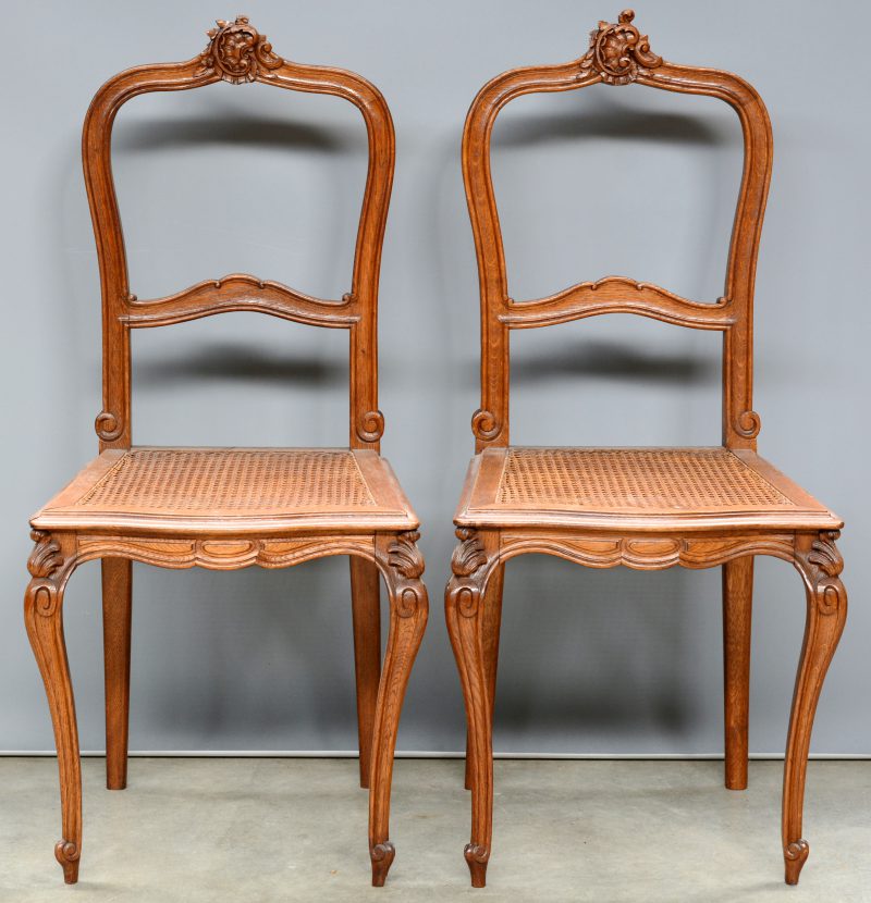 Twee gebeeldhouwde stoelen met gecanneerde zit, versierd met een rocaille op de leuning.