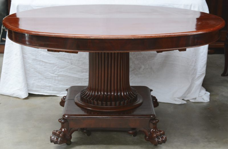 Een verlengbare ovale tafel van mahoniehout op een centrale zuilvormige poot, eindigend in vier leeuwenpoten en op wieltjes.