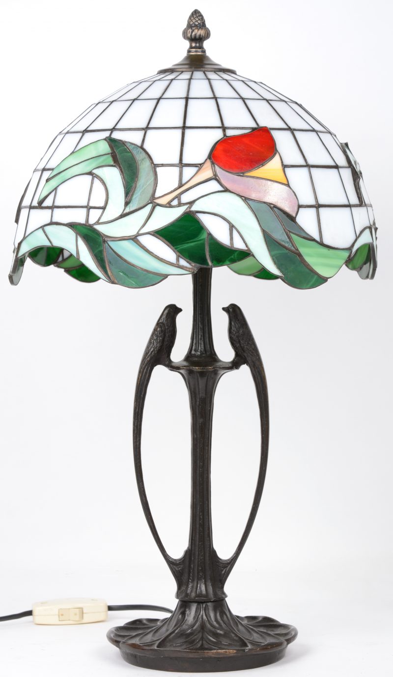 Een schemerlamp op bronzen voet, versierd met twee vogeltjes en met een kap van glas in lood in de geest van Tiffany, versierd met tulpen.