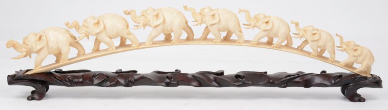 Een gesculpteerde slagtand in de vorm van een rij van zeven olifantjes. Chinees werk. Met gesculpteerd ijzerhouten sokkel.