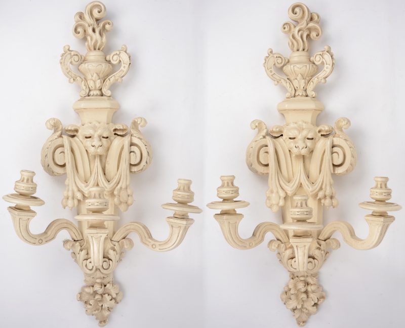 Een paar wandkandelaars van witgepatineerd hout met telkens drie lichtpunten in barokke stijl.