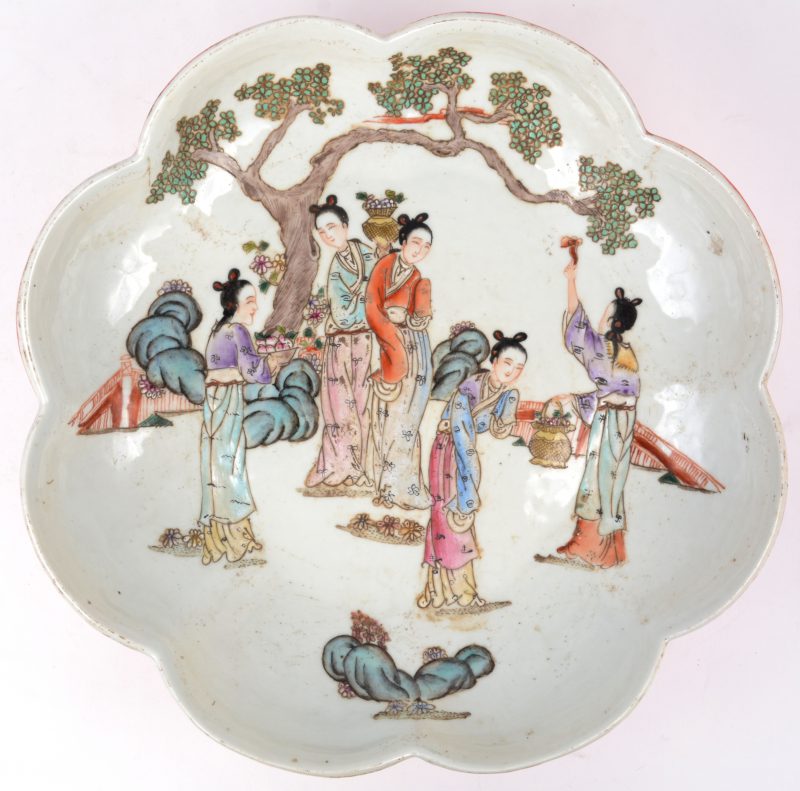 Een Chinese  diepe schaal op voet met gelobde rand, versierd met een decor van vrouwen aan een kerselaar. Onderaan gemerkt.