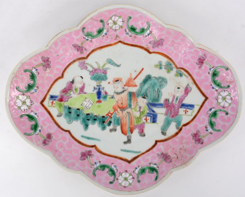 Een schaaltje op voet van Chinees porselein in gelobde ruitvorm met een famille rosedecor van personages in een landschap. Onderaan gemerkt.