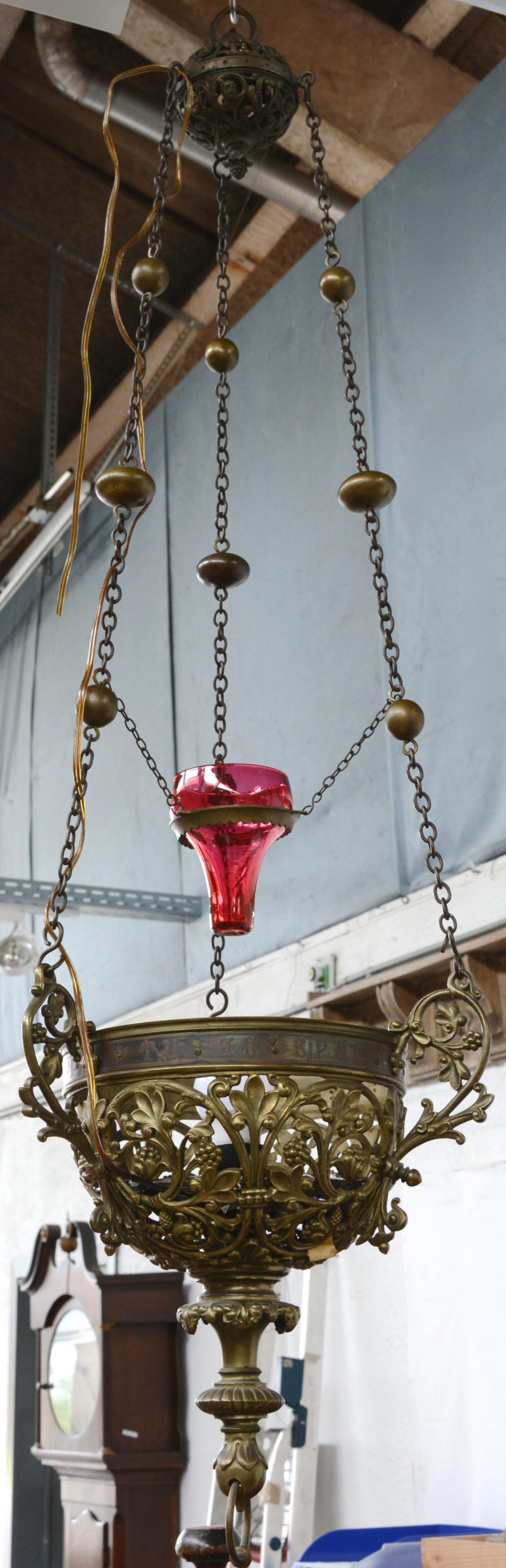 Een bronzen godslamp met opengewerkte bladermotieven en een rood glazen kapje.