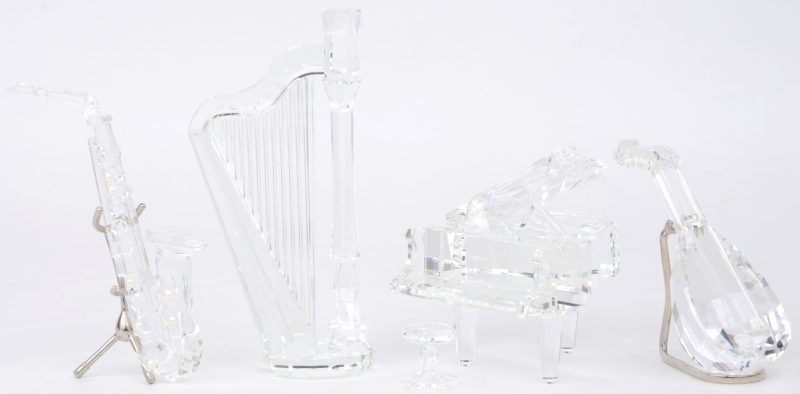 Een lotje muziekinstrumenten van geslepen kleurloos kristal, bestaande uit een vleugelpiano met krukje, een harp, een mandoline en een saxofoon. De twee laatsten met metalen staandertje.