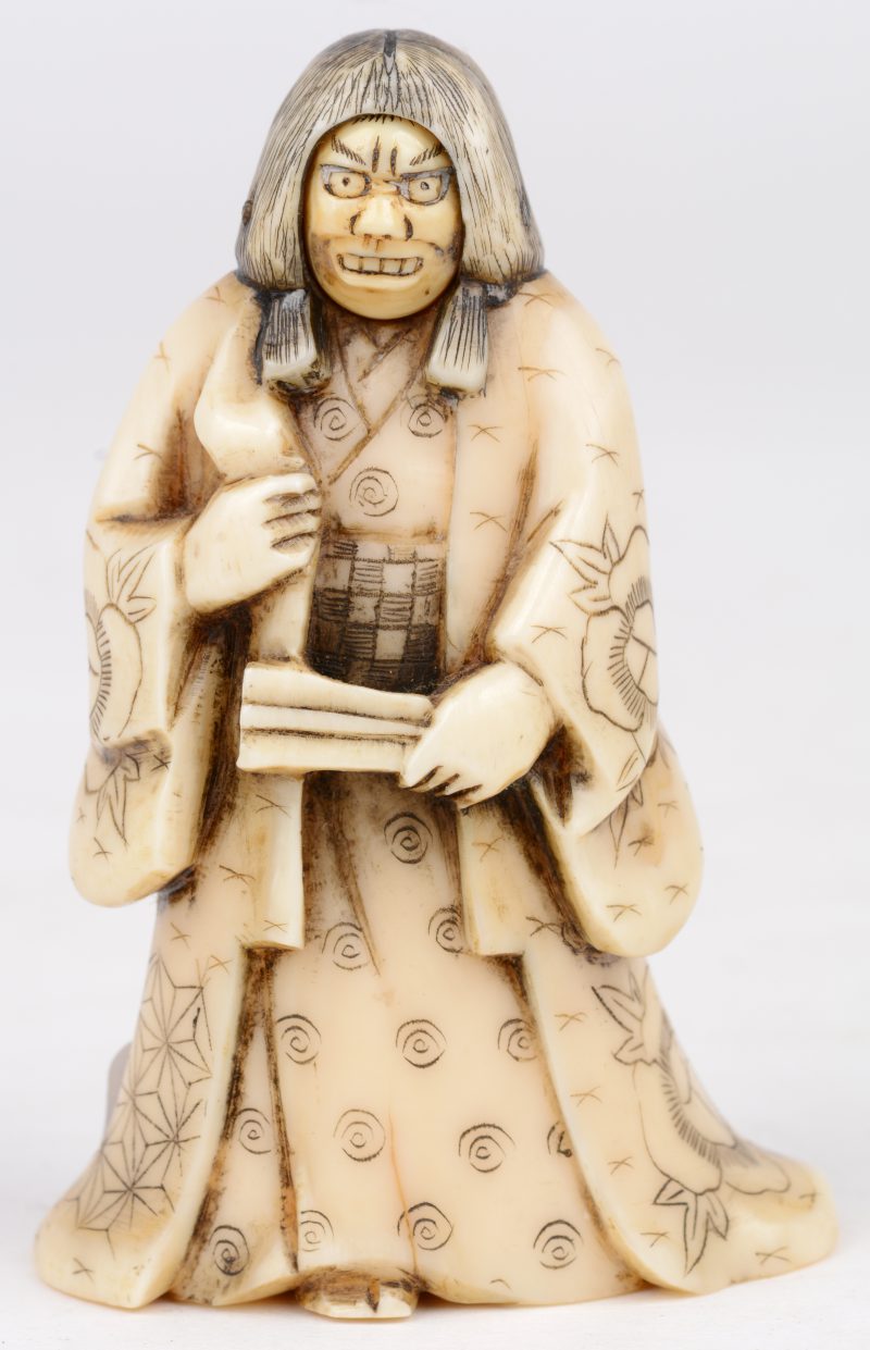 “No-akteur”. Okimono van gebeeldhouwd ivoor met tuimelend gezichtje. Japans werk omstreeks 1900. Onderaan gemerkt.