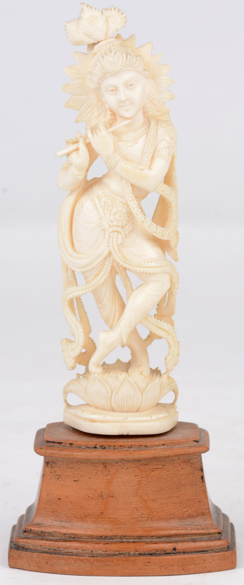 Fluitspelende “God Krishna” van gebeeldhouwd ivoor. Op houten sokkel. India, eerste helft XXste eeuw.