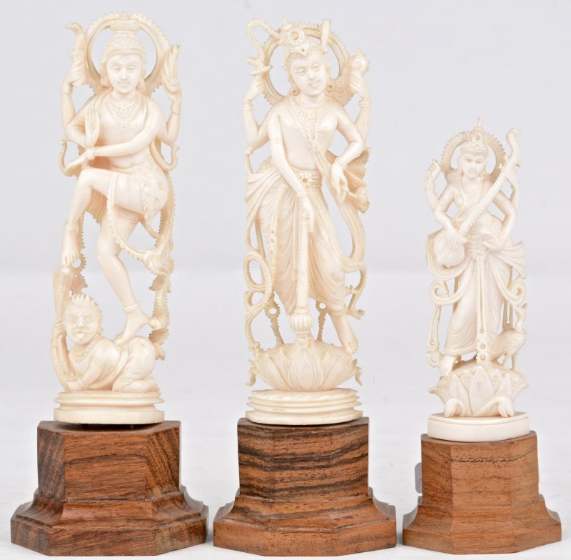“God Vishnu” en “Godin Kali op God Shiva” en “Godin Saraswati”. Drie beeldjes van gesculpteerd ivoor. Indisch werk, eerste helft XXste eeuw. Op houten sokkeltje.