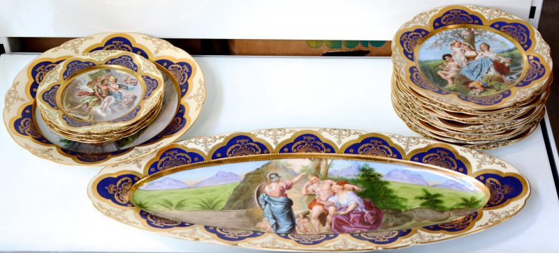 Een servies van meerkleurig en verguld porselein met decors van personages in landschappen, bestaande uit negen grote borden, vier kleine borden, een grote ronde en een grote ovale schotel. Onderaan gemerkt ‘CVM’.