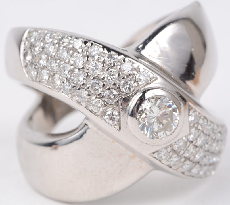 Een 18 karaats wit gouden ring bezet een centrale diamant van ± 0,25 ct. en  briljanten met een gezamenlijk gewicht van ± 0,60 ct.