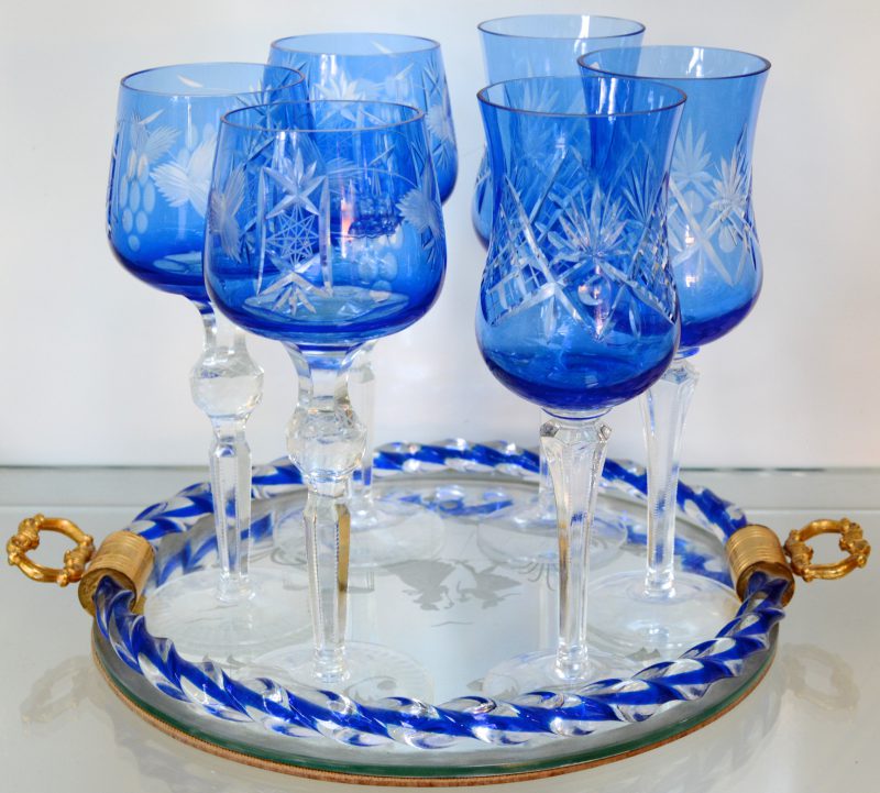 Twee reeksen van drie glazen van geslepen blauw kristal. Op glazen spiegeldienblaadje.