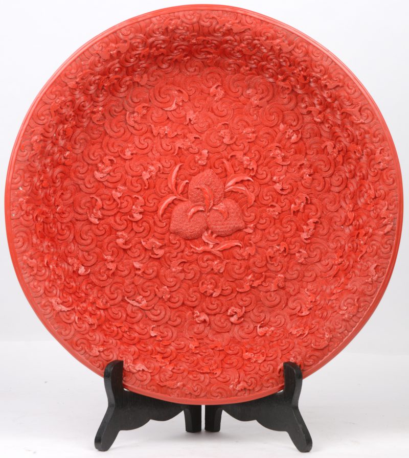Een schotel van Chinese rode lak met een reliëfdecor van vruchten en vleermuizen. Onderaan gemerkt.