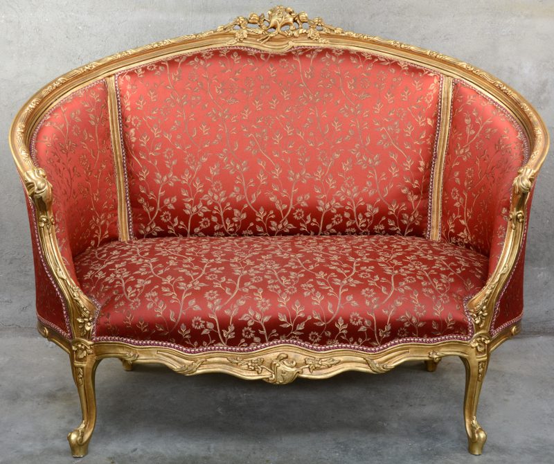 Een zitbank van gesculpteerd en goudgepatineerd hout in Lodewijk XV-stijl met rode bekleding.