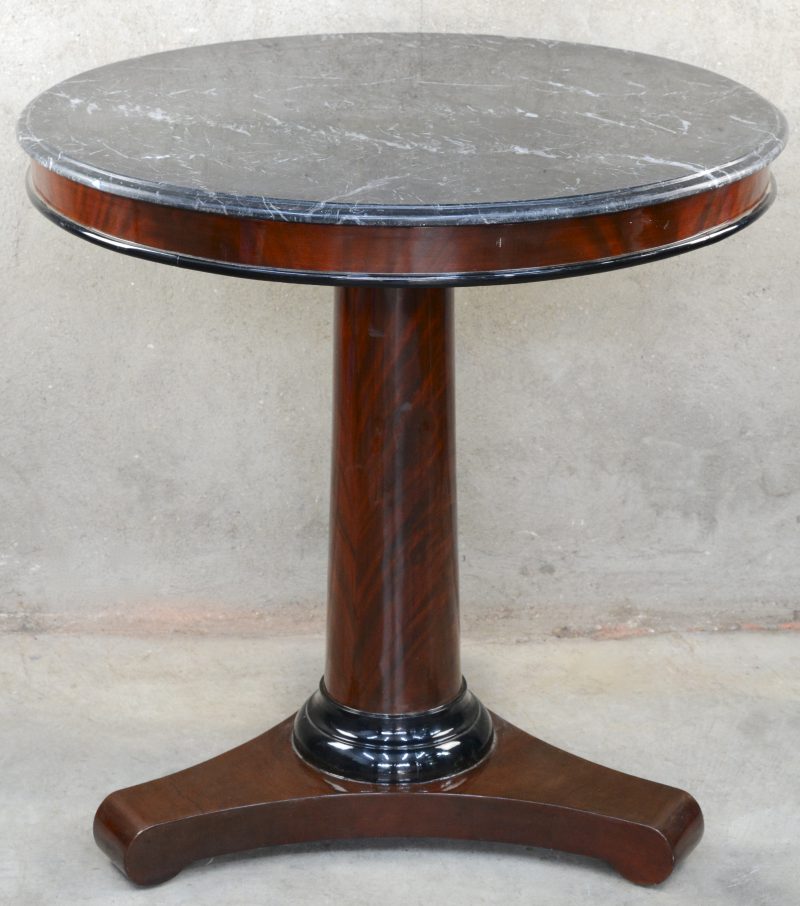 Een ronde tafel van mahoniehoutfineer met een zwart marmeren blad.