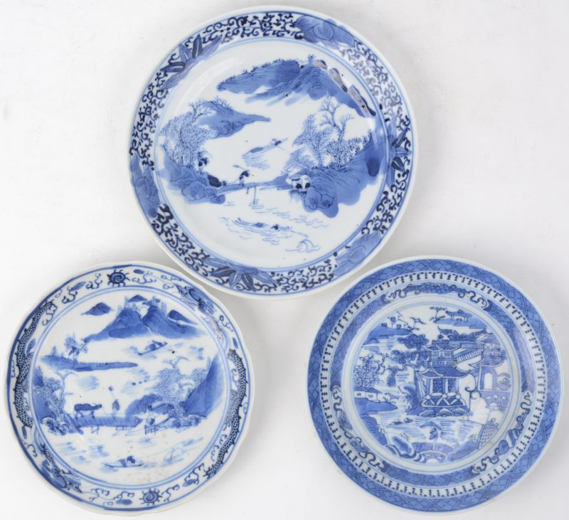 Een lot van drie verschillende schoteltjes van blauw en wit Chinees porselein met landschapsdecors.