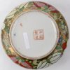 Een dekseldoos van Chinees porselein met een meerkleurig decor van de hofhouding op het deksel en vruchten op gouden fond op het recipiënt. Onderaan gemerkt.