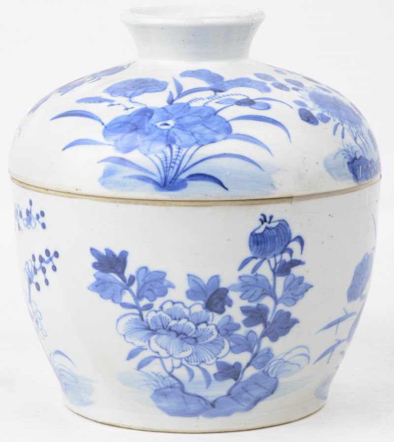 Een dekselpot van Chinees porselein met een blauw en wit decor van bloemen en bloeiende struiken.
