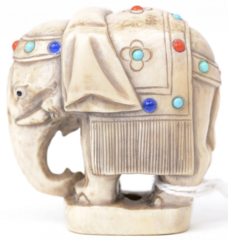 Een netsuke van gesculpteerd Japans ivoor in de vorm van een olifant, versierd met ingewerkte stukjes koraal en aquamarijn. Eerste kwart XXe eeuw. Onderaan gesigneerd.