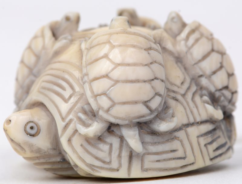 “Schildpad met jongen op haar schild”. Een netsuke van gesculpteerd ivoor. Eerste kwart XXe eeuw. Onderaan gesigneerd.