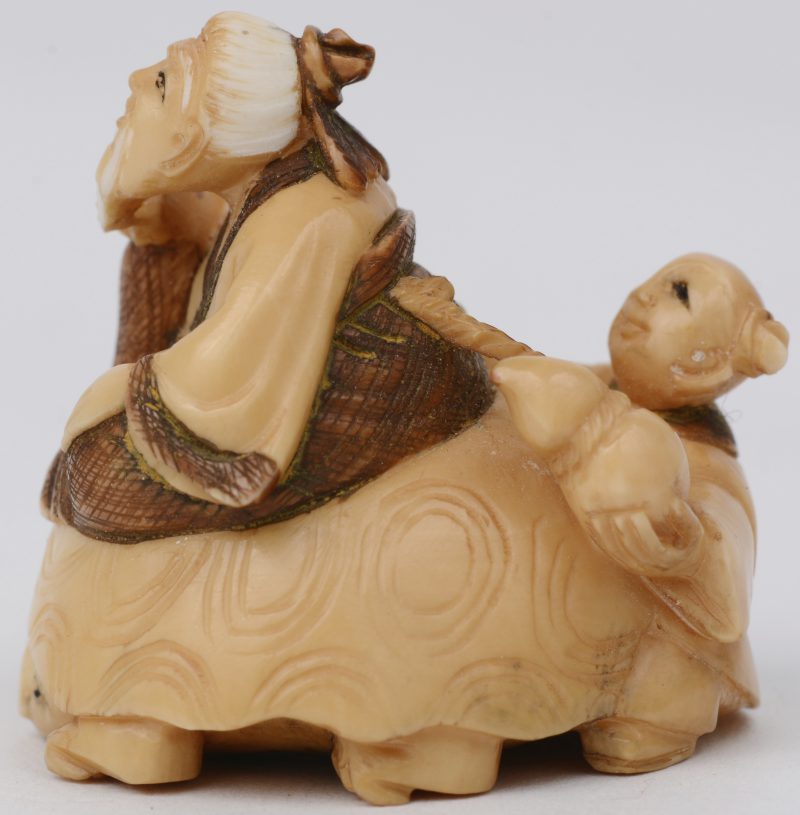“Wijze en kind op schildpad”. Een netsuke van gesculpteerd ivoor met gepolychromeerde accenten. Onderaan gesigneerd. Eerste kwart XXe eeuw.