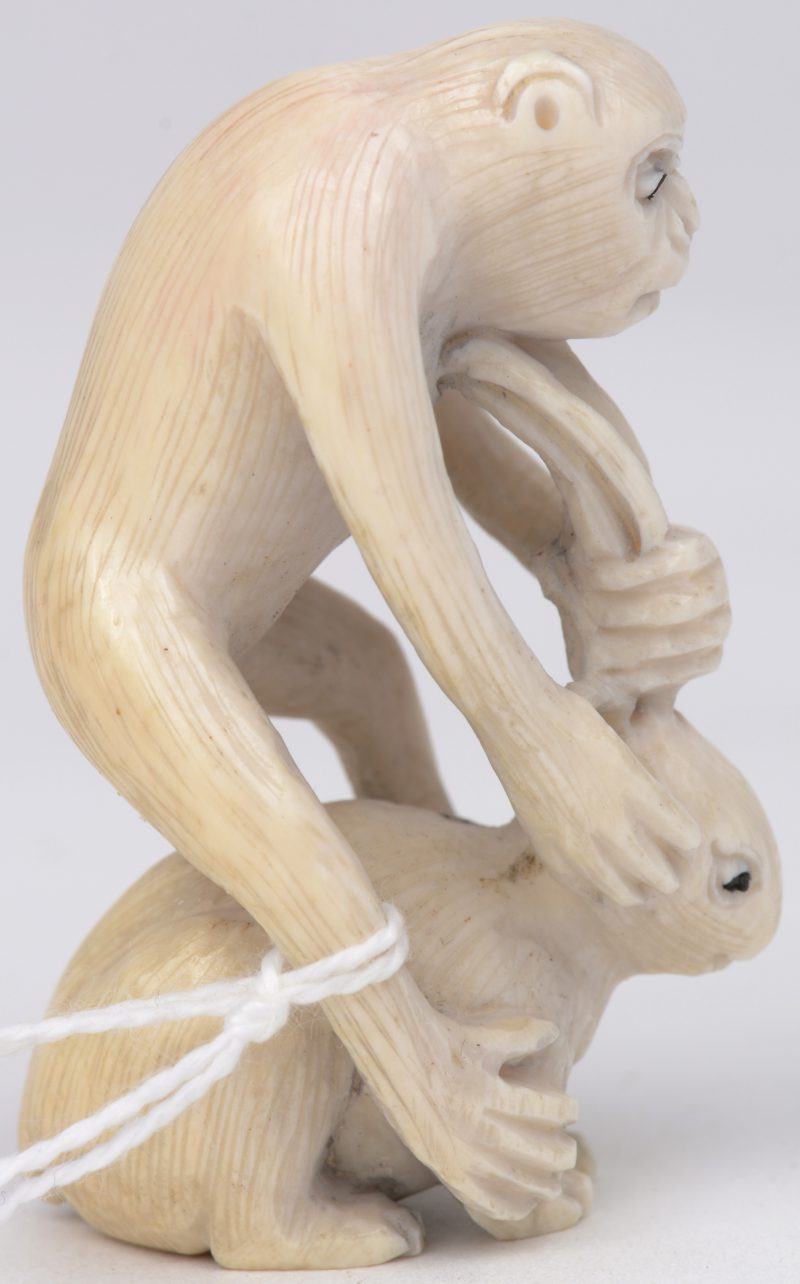 “Aap op konijn”. Een netsuke van gesculpteerd ivoor. Onderaan gesigneerd. Eerste kwart XXe eeuw.