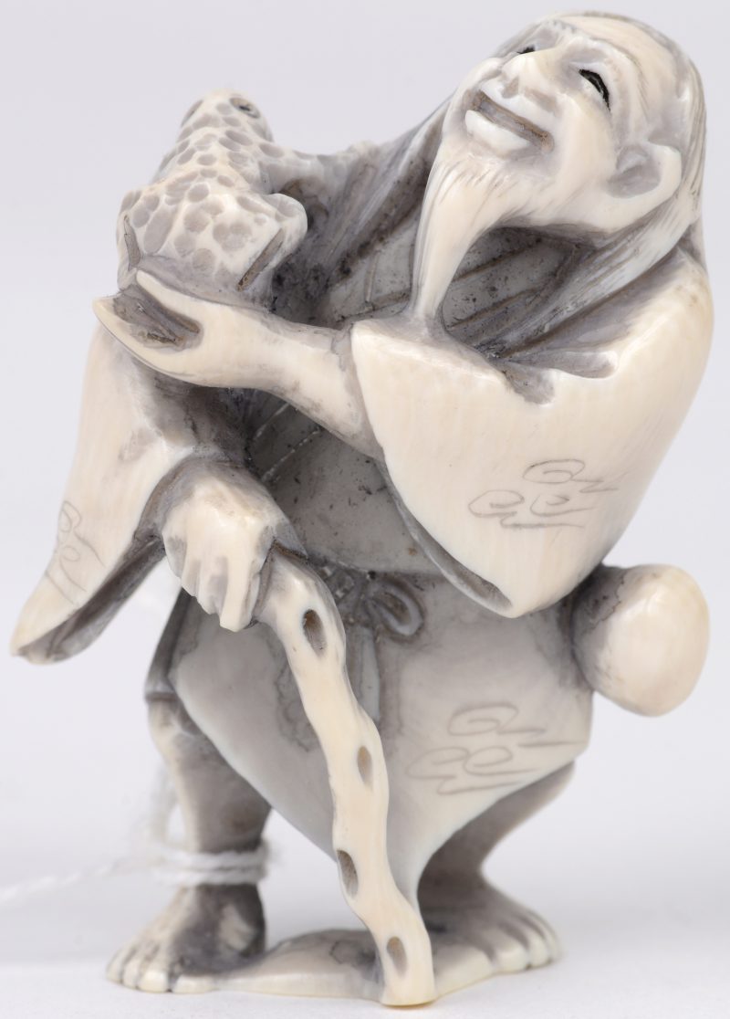 “Man met taikostokken”. Een netsuke van gesculpteerd ivoor. Onderaan gesigneerd. Eerste kwart XXe eeuw.