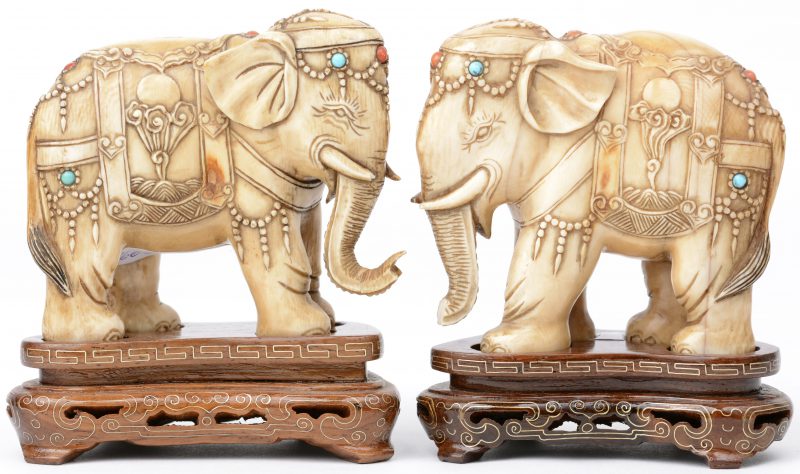 Een paar olifanten van gesculpteer ivoor, versierd met koraal en aquamarijn. Met houten sokkeltjes. Eén slurf licht beschadigd.