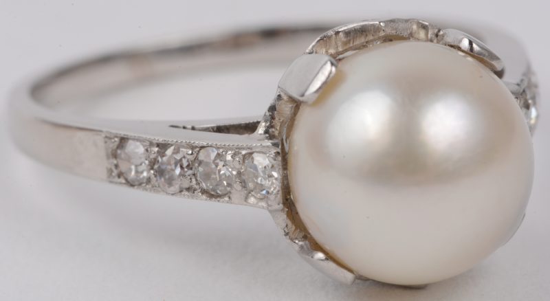Een 18 karaats wit gouden ring bezet met briljanten met een gezamenlijk gewicht van ± 0,20 ct. en een parel.
