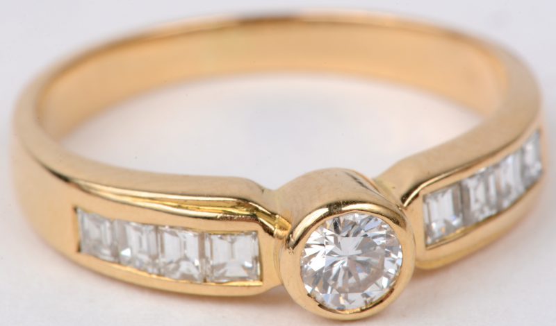 Een 18 karaats geel gouden ring bezet met een centrale briljant van ± 0,20 ct. en met diamantbaguetten met een gezamenlijk gewicht van ± 0,30 ct.