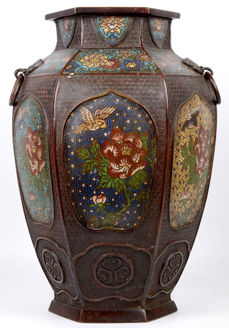 Een zeshoekige vaas van cloisonné op brons met een decor van bloemen en vogels en met ringen als handvatten. Onderaan gestempeld. Omstreeks 1900.