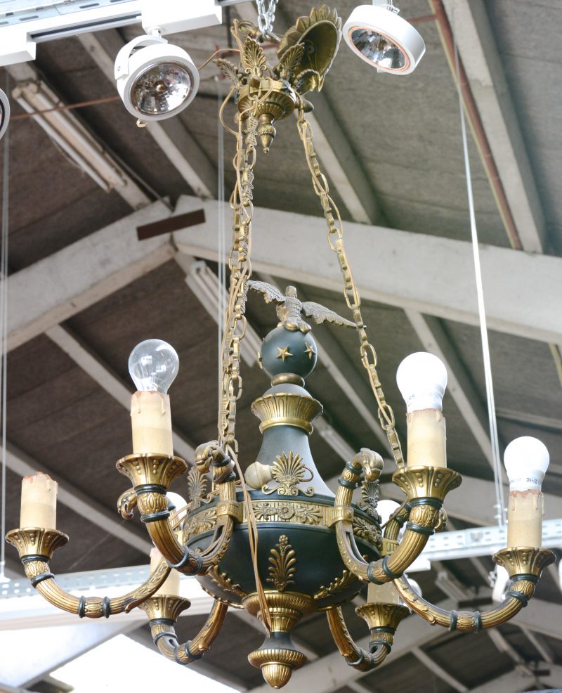 Een bronzen luchter met vijf vergulde lichtarmen, centraal getooid met een vogel op een bal. Tijdperk Empire.
