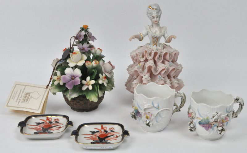 Een divers lot porselein bestaande uit een Saksische dame, twee Imari asbakjes, twee kopjes en een bloemstuk.