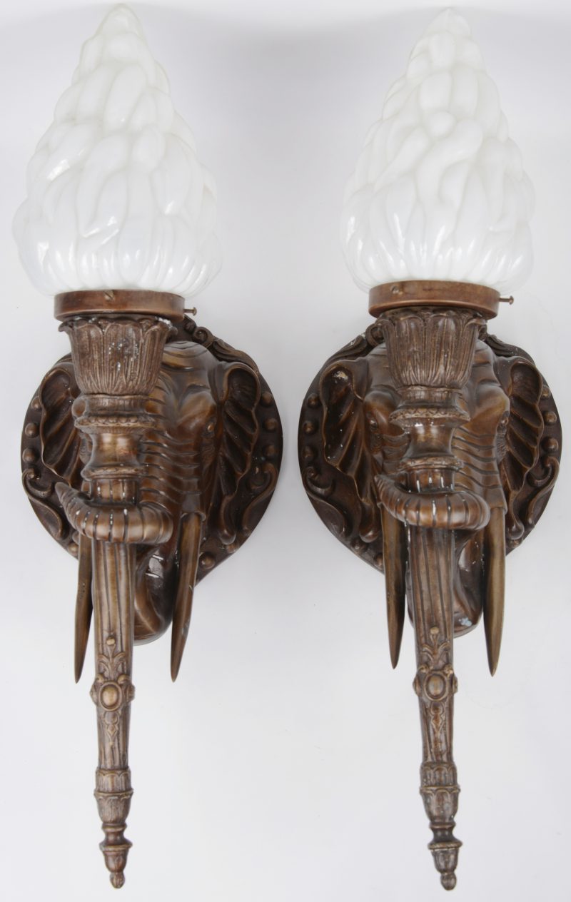 Een paar bronzen wandlampen in de vorm van olifantskoppen met glazen kappen in de vorm van vlammen.