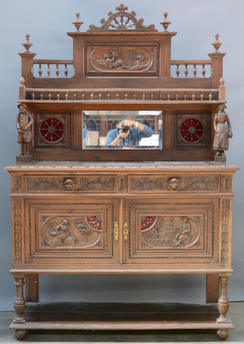 Een eikenhouten buffetkast met opzet, gedragen door twee gebeeldhouwde figuren. In het opzet een spiegel tussen twee wielen en bovenaan een galerijtje. Onderaan twee deuren en twee laden en een marmeren blad.