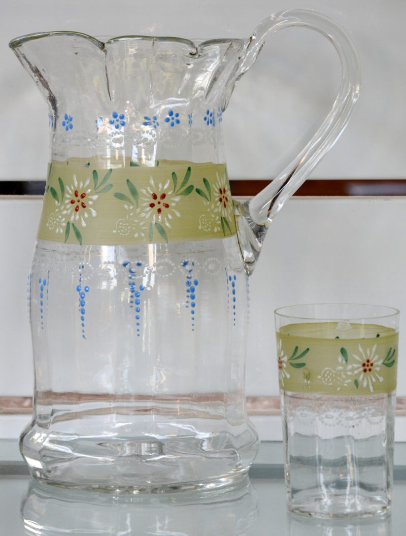Een mondgeblazen glazen schenkkan met glas, versierd met een bloemendecor. Omstreeks 1900.