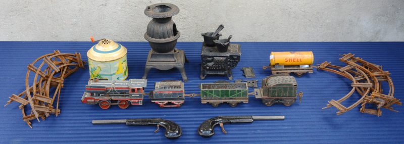 Een lot speelgoed bestaande uit twee gietijzeren kacheltjes met toebehoren en blikken speelgoed bestaande uit een locomotief en 4 wagons met sporen (verroest), twee speelgoedpistooltjes (KB Paris) en een muzikale draaimolen.