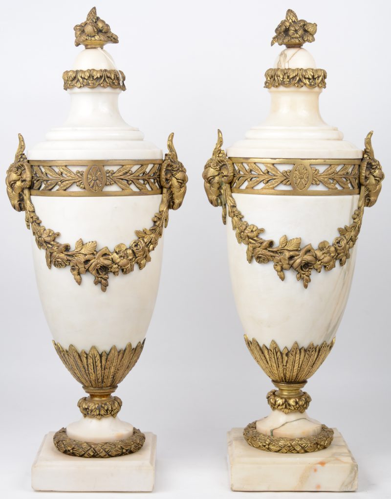 Een paar cassolettes van wit marmer, versierd met bronzen monturen in de vorm van ramskoppen en bloemenguirlandes.
