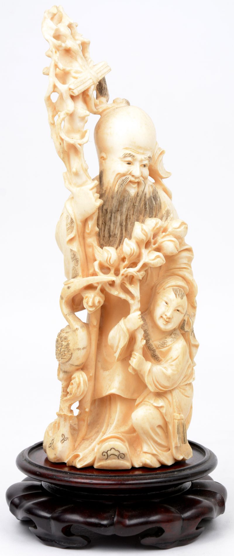 “Oude man met staf, een jongeman en een reiger”. Een beeld van gesculpteerd ivoor. Onderaan gemerkt. Met houten sokkel.