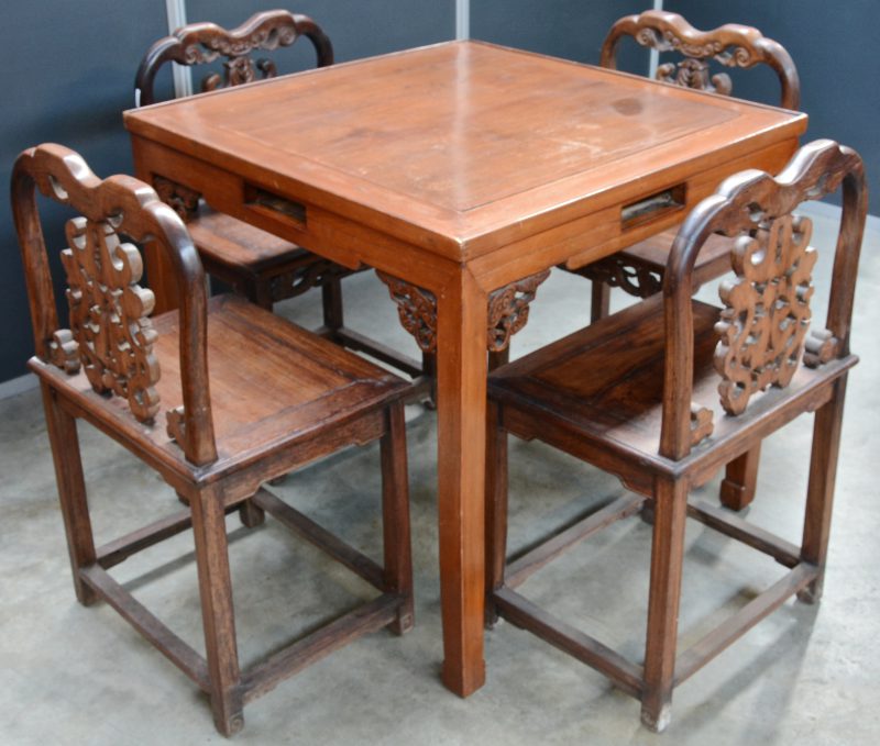 Een Chinese tafel met vier bijpassende stoelen van gesculpteerd tropisch hout.