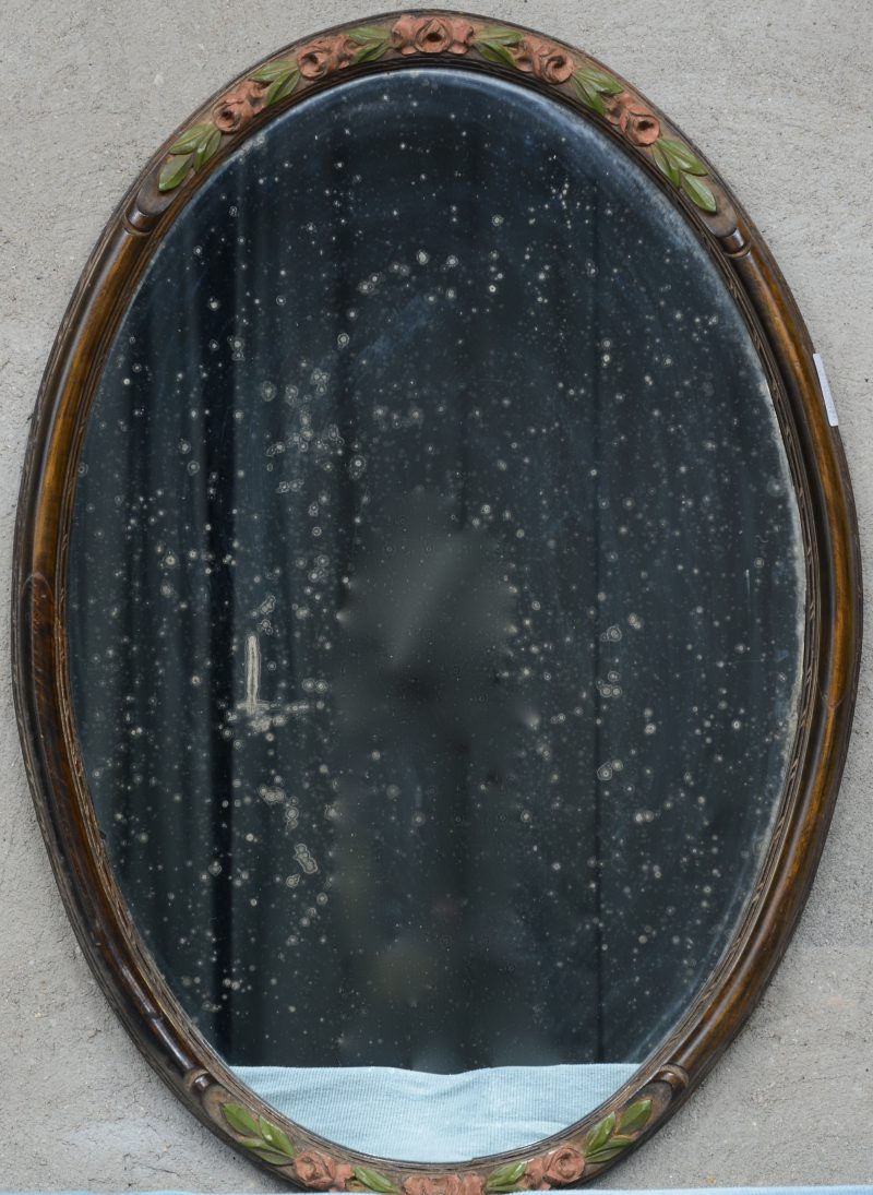 Een ovale spiegel van gepolychromeerd hout, versierd met meerkleurige roosjes.