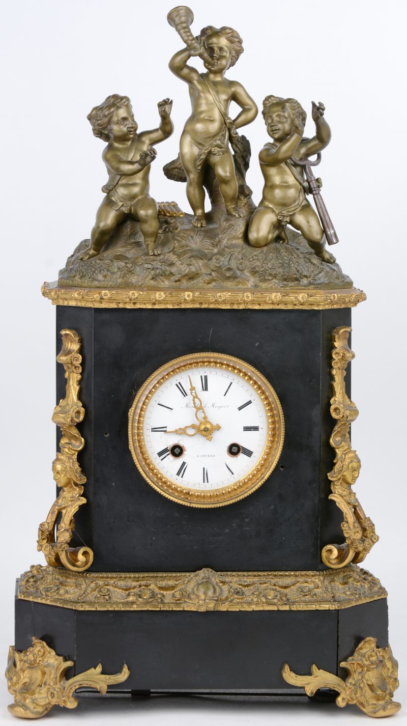 Een schouwpendule van arduin in Napoleon III-stijl, versierd met verguld brons en bovenaan getooid met drie musicerende putti.  De wijzerplaat gemerkt. Met slinger en sleutel.