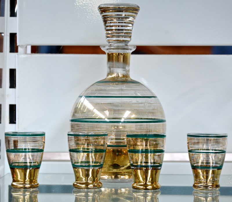 Een met goud versierd Booms glazen likeurstelletje, bestaande uit een bolle karaf en vier glaasjes.