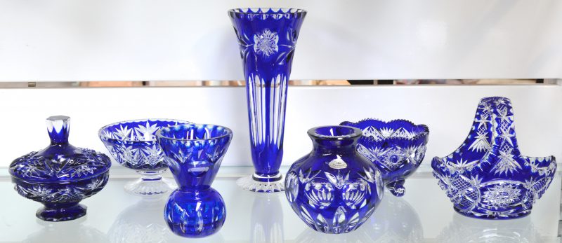 Een lot geslepen blauw Boheems kristal, bestaande uit een bolle vaas, een kelkvaas, een coupe op voet, een vaas op voet, een bonbonnière, een mandje en een fruitschaal.