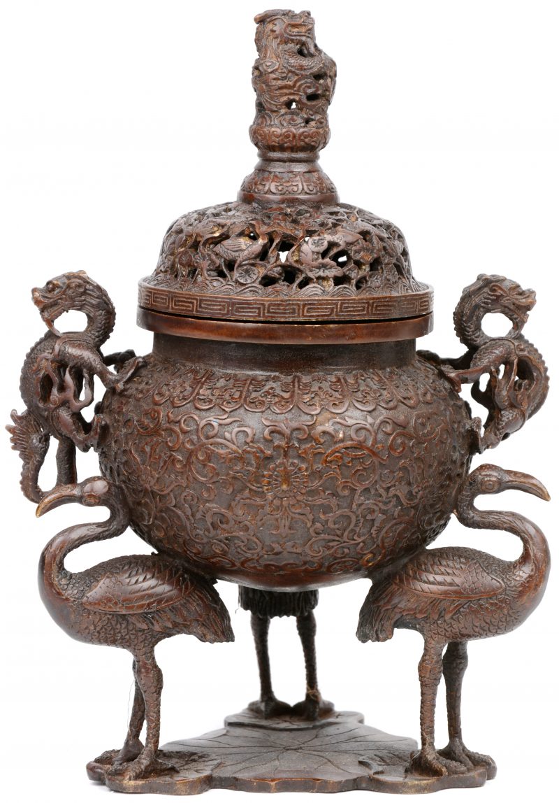 Een Chinese bronzen koro met een opengewerkt deksel, versierd met vogels en bloemen, getooid door een draak? De handvatten eveneens in de vorm van draken en het geheel gedragen door drie kraanvogels op leliebladeren. Gemerkt onderaan.