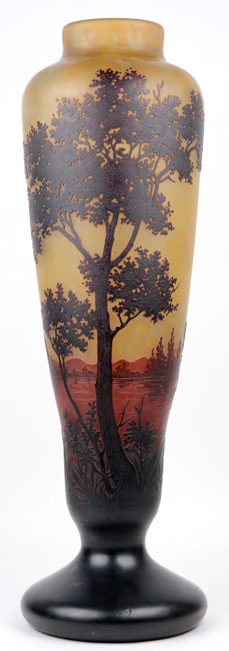 Een grote glazen vaas met een met het wiel gegraveerd landschapsdecor op een oranjebruine achtergrond, eindigend in een donkere voet. Voluit gemerkt en met het kruis van Lotharingen. Begin XXe eeuw.
