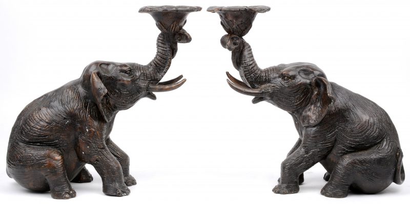 Een paar bronzen kandelaars in de vorm van zittende olifanten met een bloem.