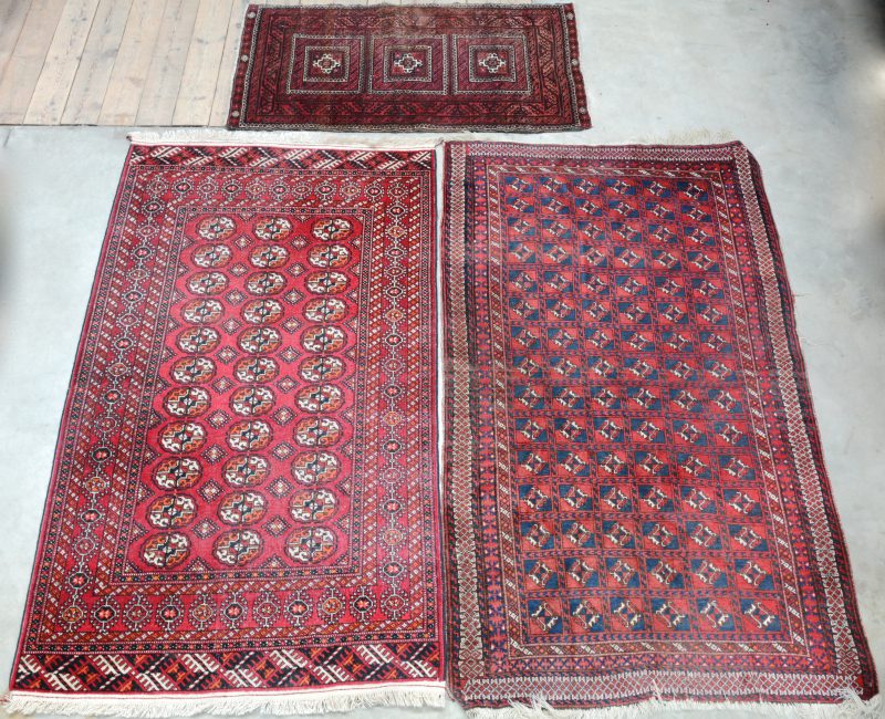 Een lot van drie handgeknoopte Pakistaanse wollen karpetjes. Eén met scheur.