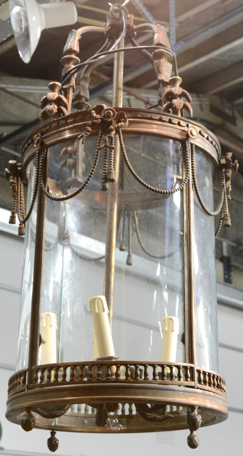 Een ronde hallantaarn van brons met vier lichtpunten, versierd met strikken.