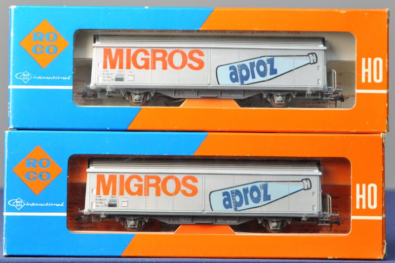 Twee gesloten goederenwagons ‘Migros Aproz Mineralwasser’ van de Zwitserse spoorwegen voor spoortype HO. In originele dozen.